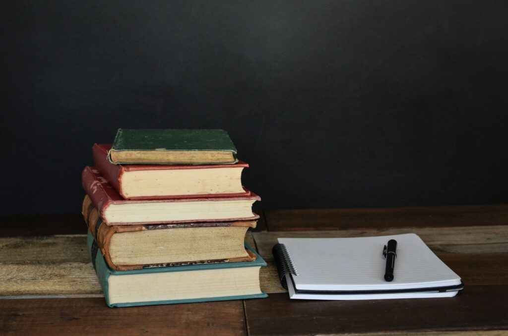 Une pile de livres se trouve sur une table. à côté d'un cahier de notes sur lequel repose un crayon.